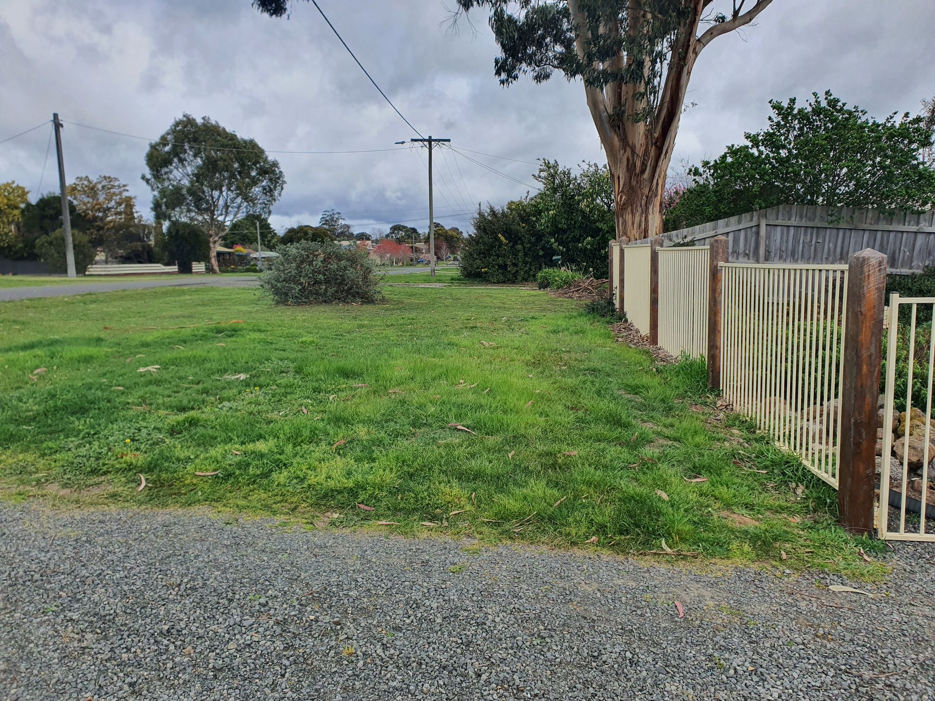Grassy yard with a gravel path, fence, and trees under an overcast sky — JKR Garden Maintenance Services in Ballan, VIC
