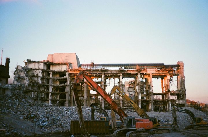 Orange excavators stand before a partially demolished building at sunset.