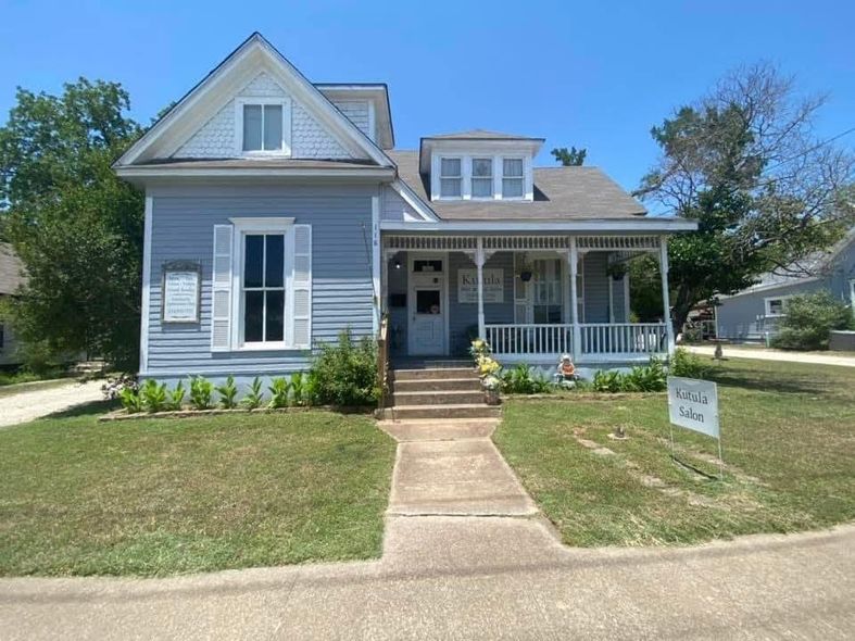 Blue Victorian house with white trim, porch, and a sign in the yard.
