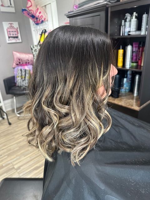 Hair with dark roots, transitioning to blonde, styled with loose curls. Salon setting.