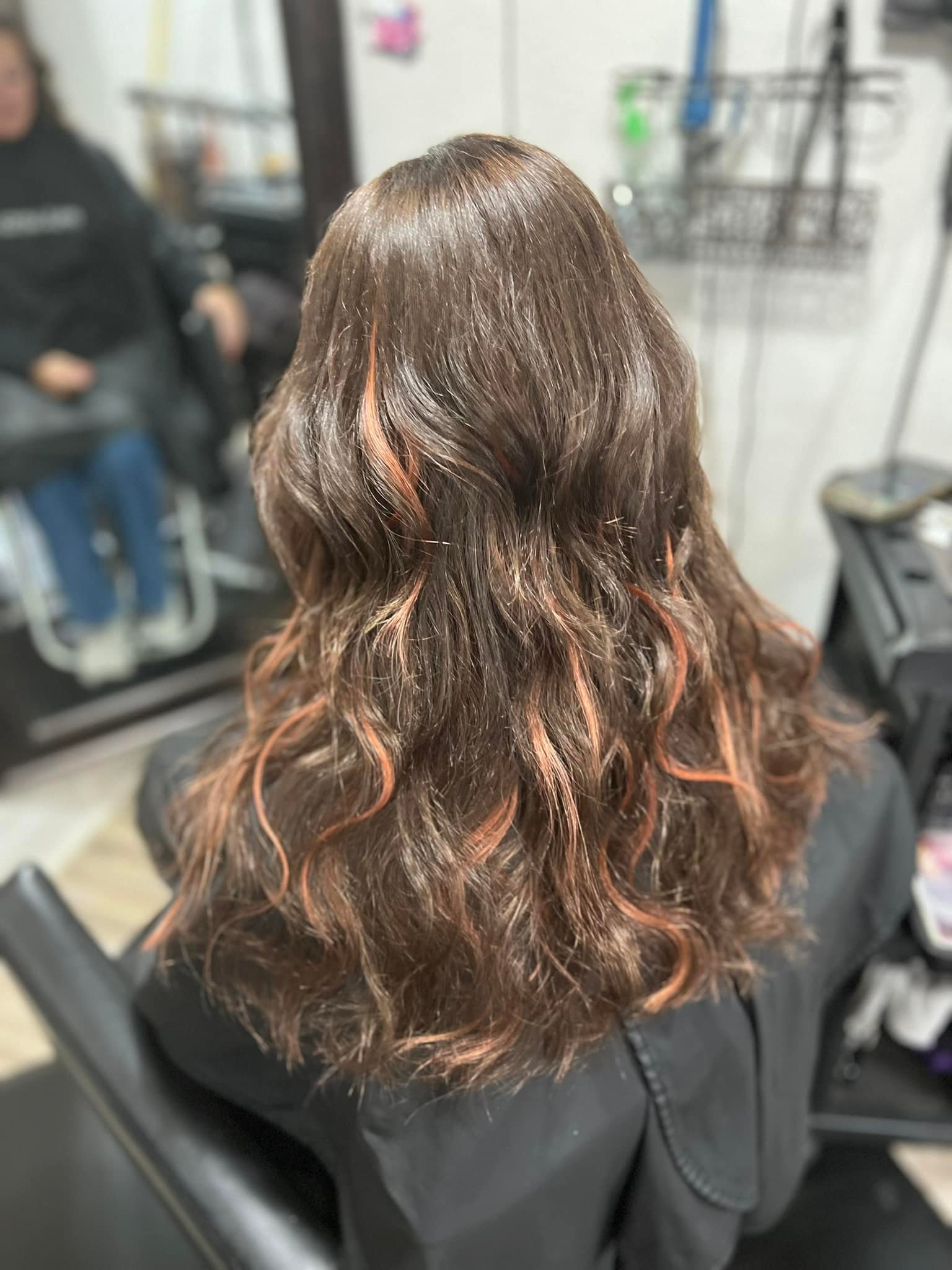 Hair styled with waves and red highlights, sprinkled with glitter. Sitting in a salon chair.