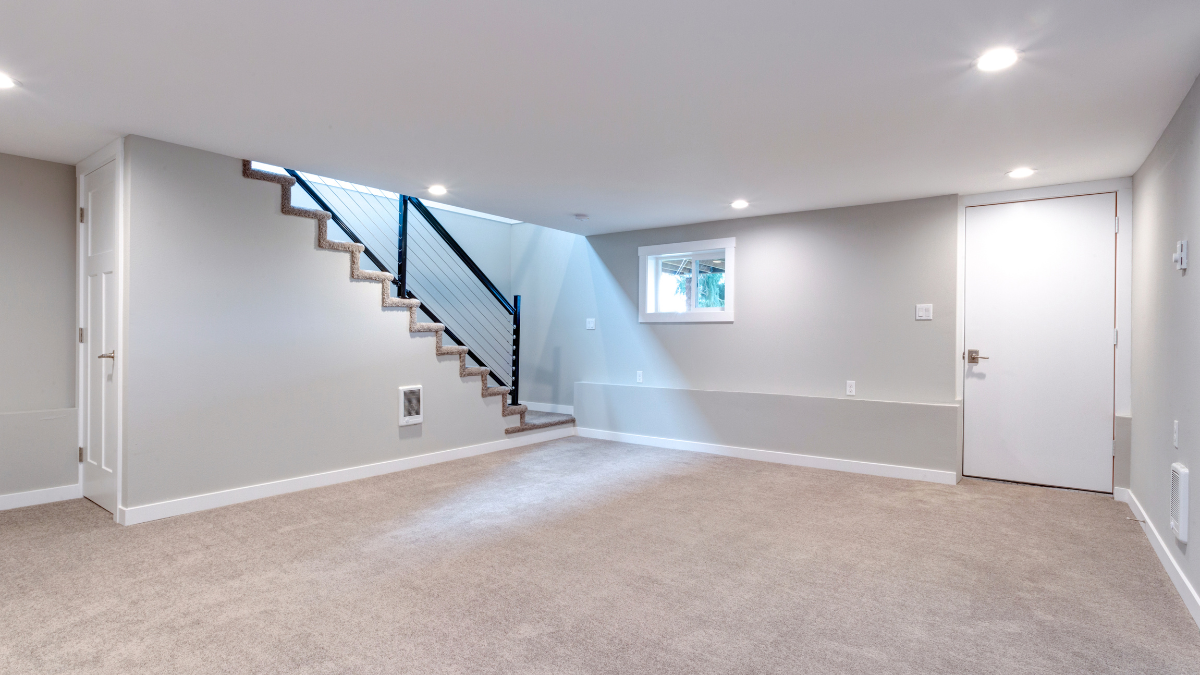 An empty basement with a staircase and a window.