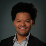 A man with curly hair is wearing a suit and smiling for the camera.