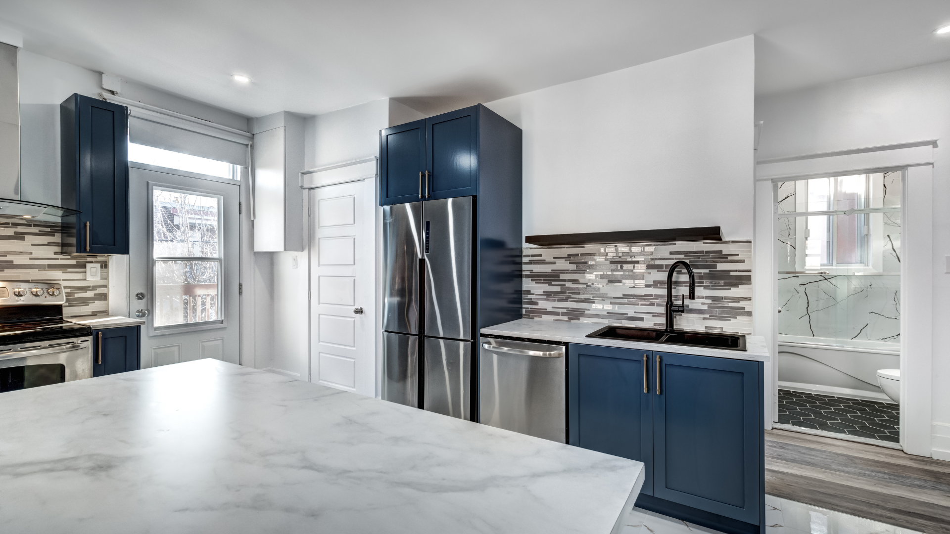 A kitchen with blue cabinets , stainless steel appliances , a sink , and a refrigerator.