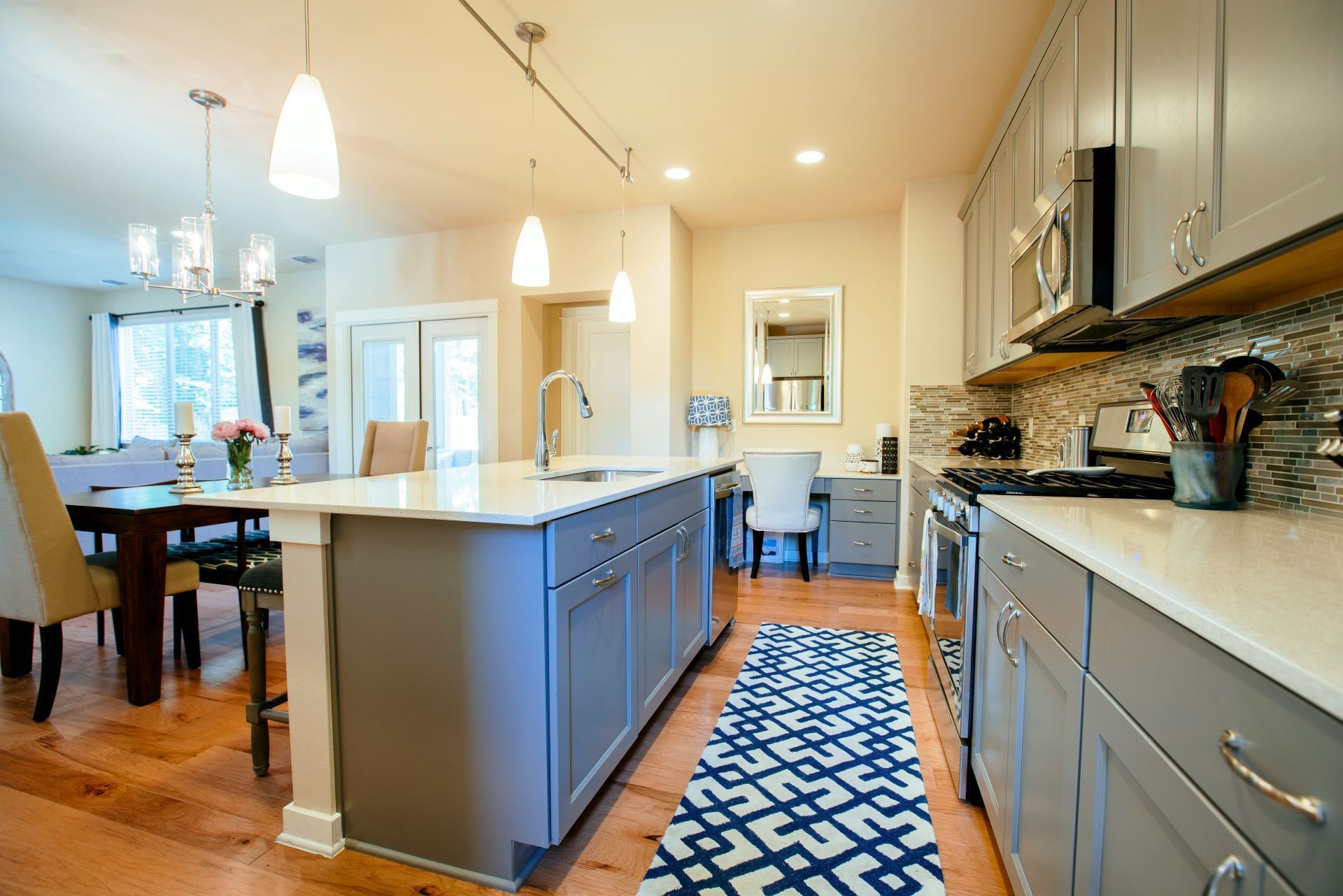 A kitchen with gray cabinets , white counter tops , and a blue rug.