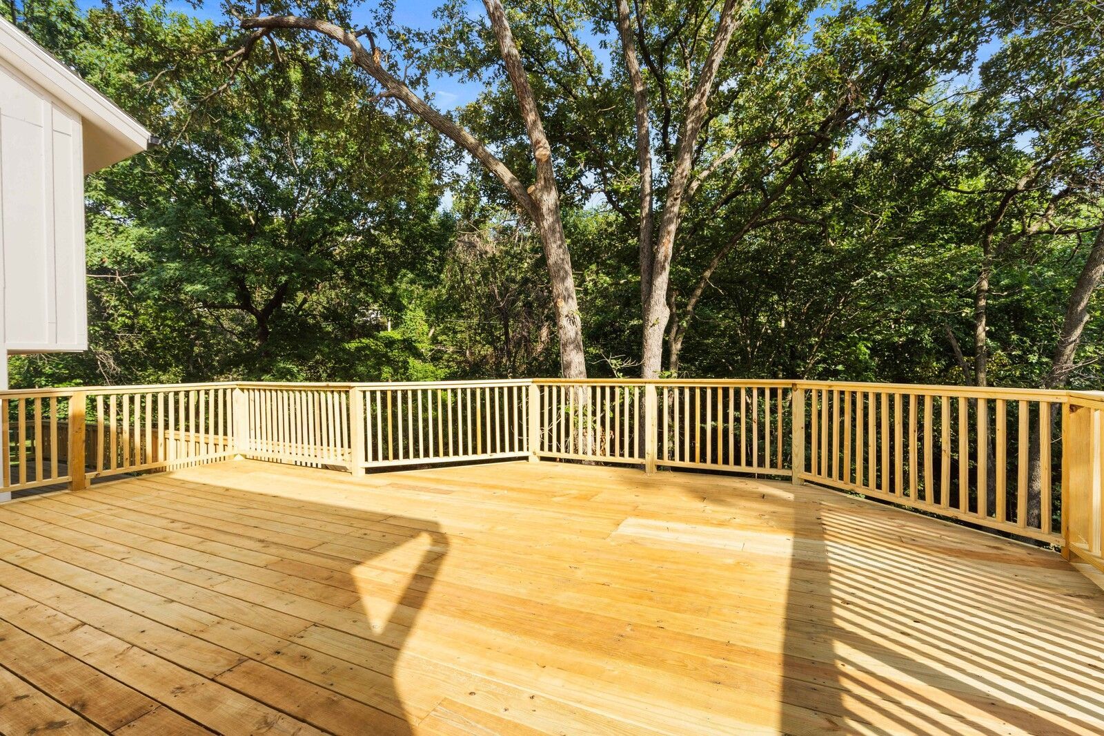 An empty wooden deck with a wooden railing and trees in the background.