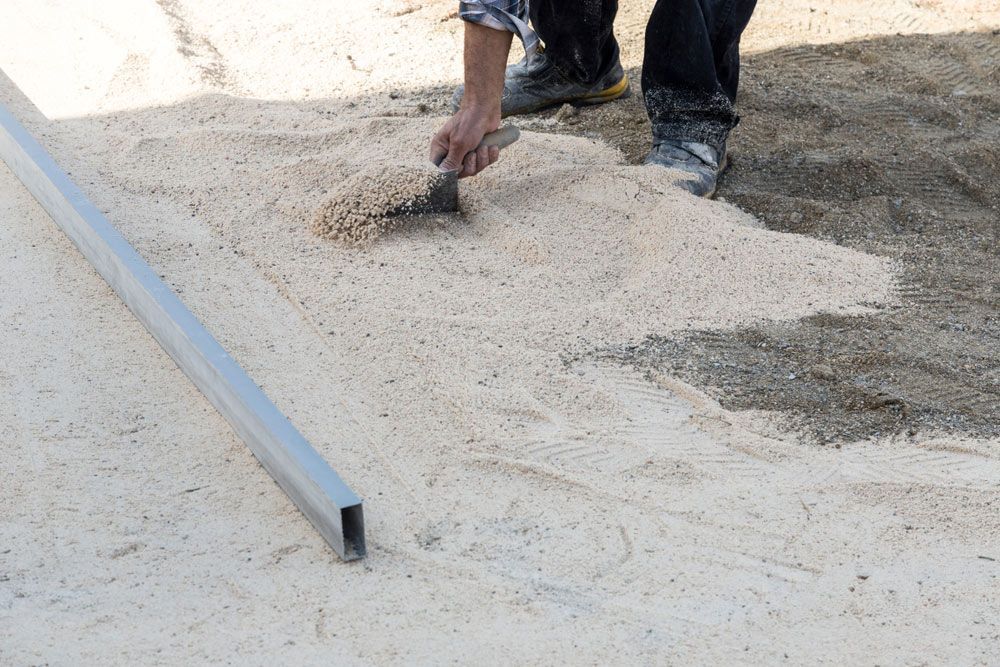 A Person Is Spreading Sand On The Ground With A Trowel — Ian Brown Sand Supplies and Tipper Hire In Port Macquarie, NSW