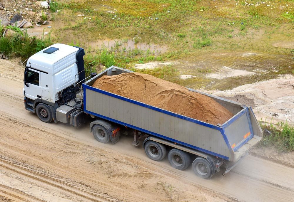 A Dump truck is Driving down a Dirt road — Ian Brown Sand Supplies and Tipper Hire In Laurieton, NSW