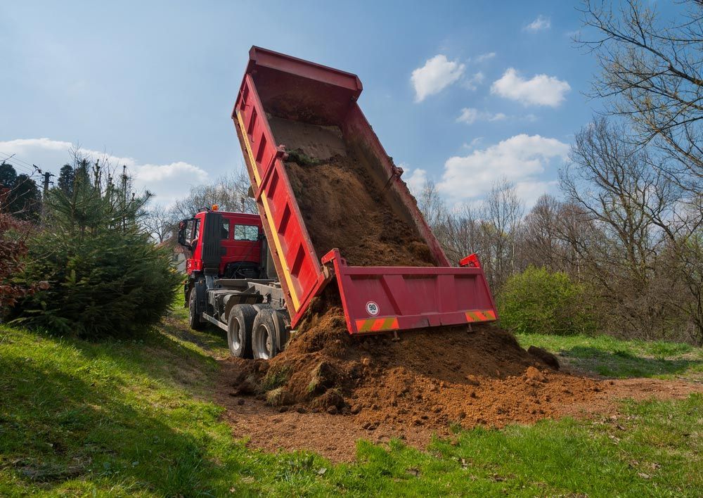 A red dump truck is Dumping dirt into a field — Ian Brown Sand Supplies and Tipper Hire In Wauchope, NSW