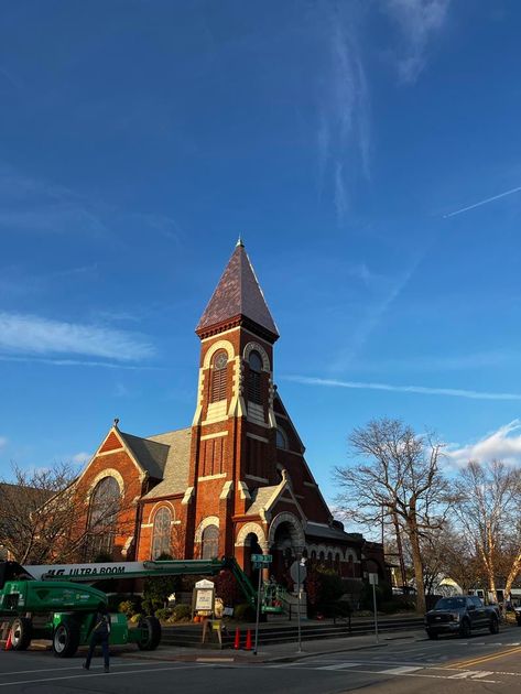 A large brick church with a steeple and a blue sky in the background