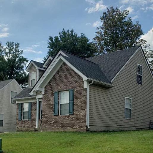 A brick house with a gray siding and blue shutters is sitting on top of a lush green lawn.