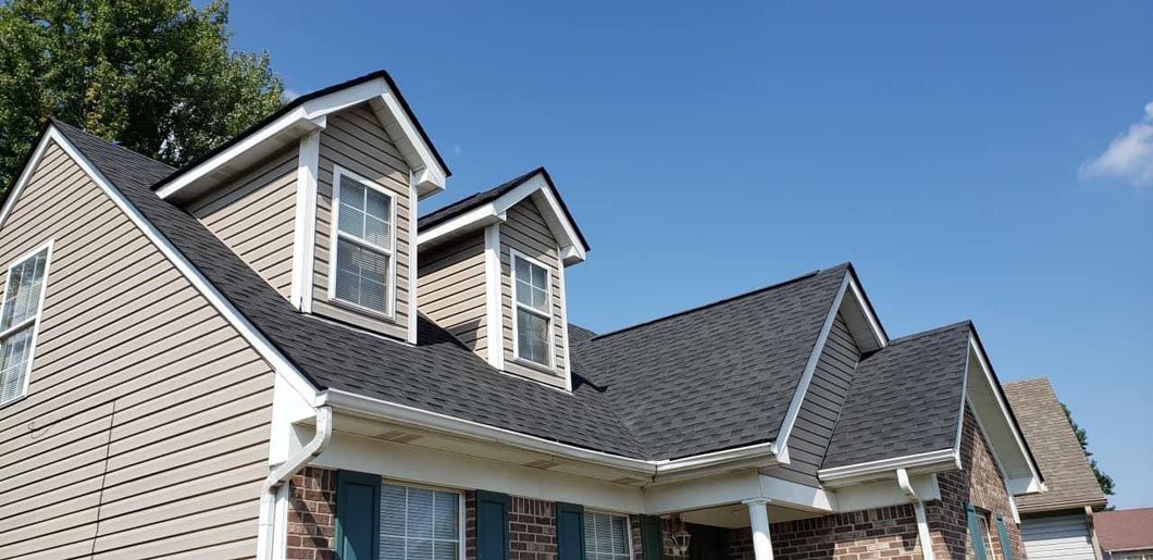 A house with a black roof and a blue sky in the background.