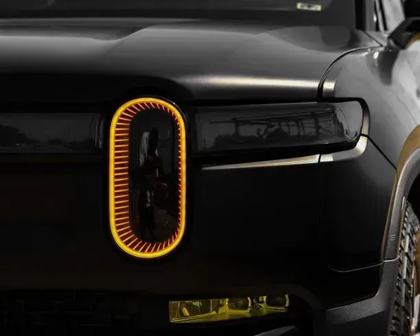 Close-up of a matte black Rivian electric truck's front with unique oval headlight and yellow fog lights.