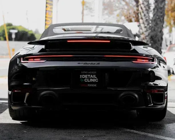 Black Porsche 911 Turbo convertible rear view, daytime, with detailing clinic logo.