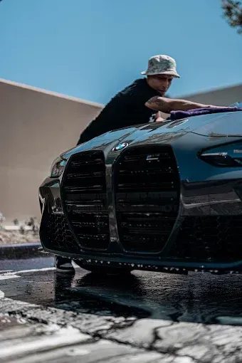 Man in black gloves polishing a black car with a yellow cloth.
