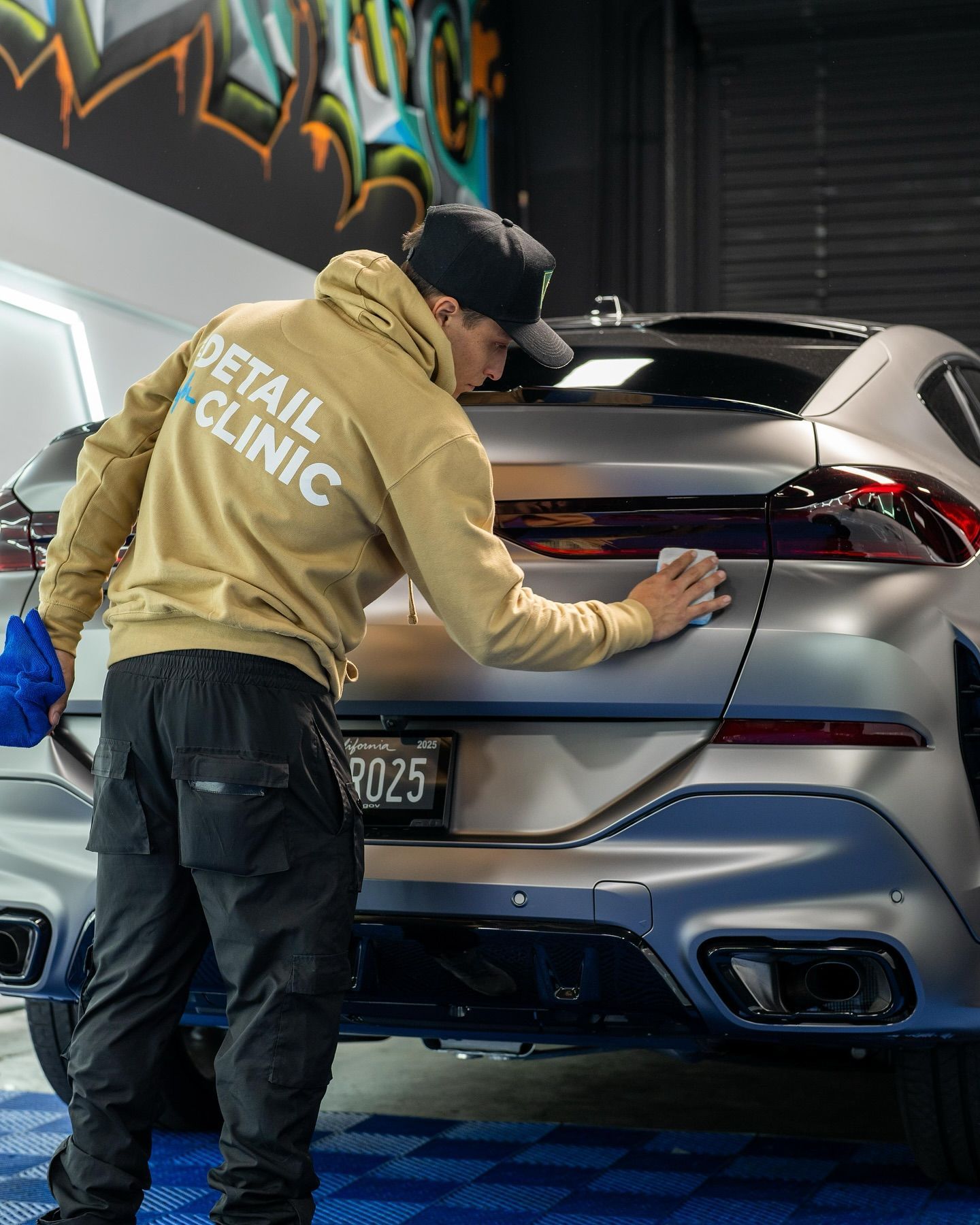 A person applying blue vinyl wrap to the hood of a car with a squeegee in a workshop.