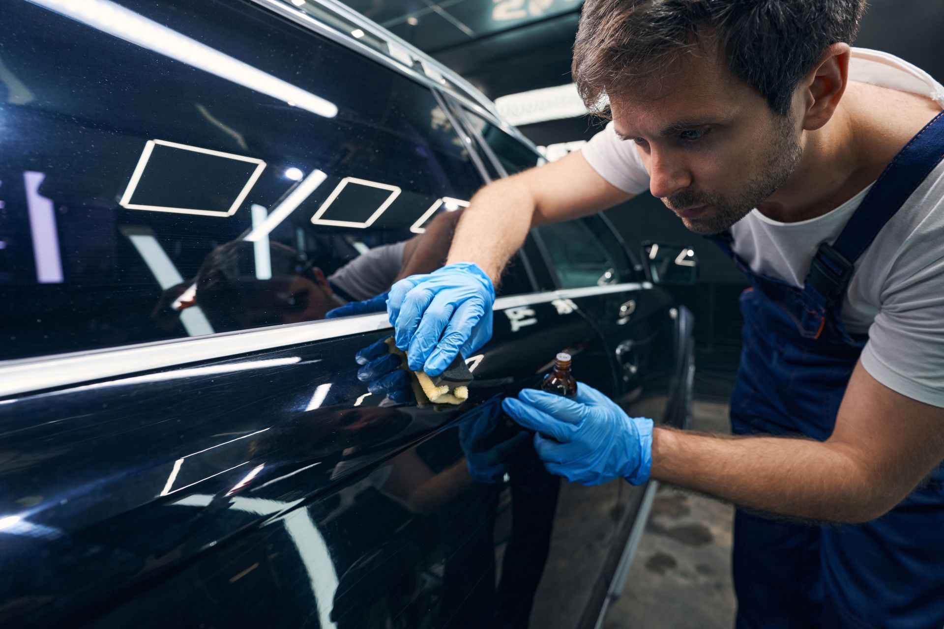 Man wearing blue gloves, cleaning a black car door handle.