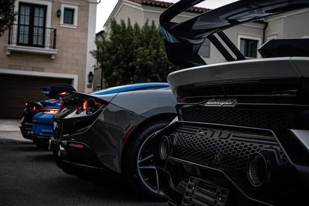 Three luxury sports cars parked on a street in front of a house.