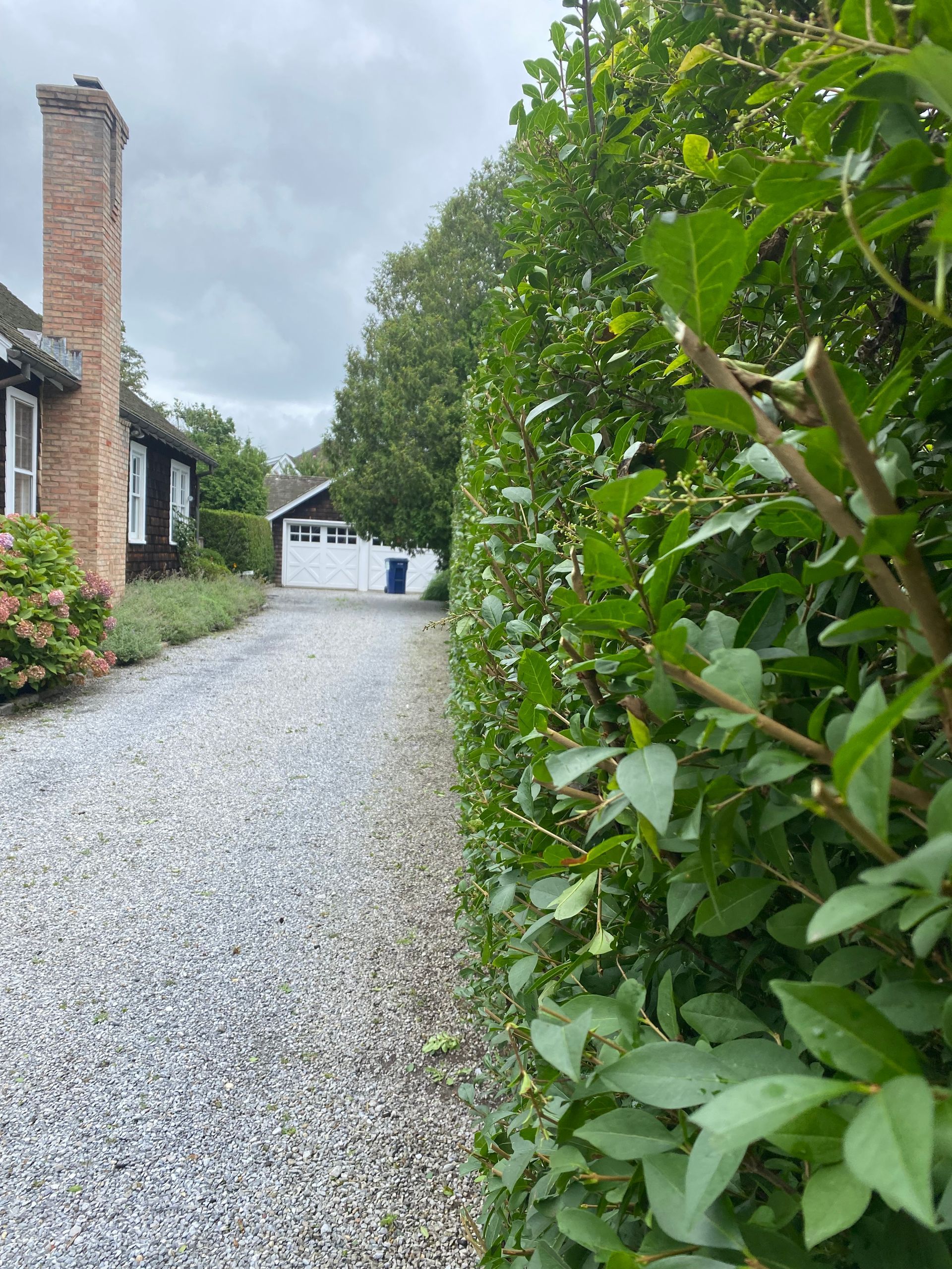 A gravel driveway leading to a house with a brick chimney.