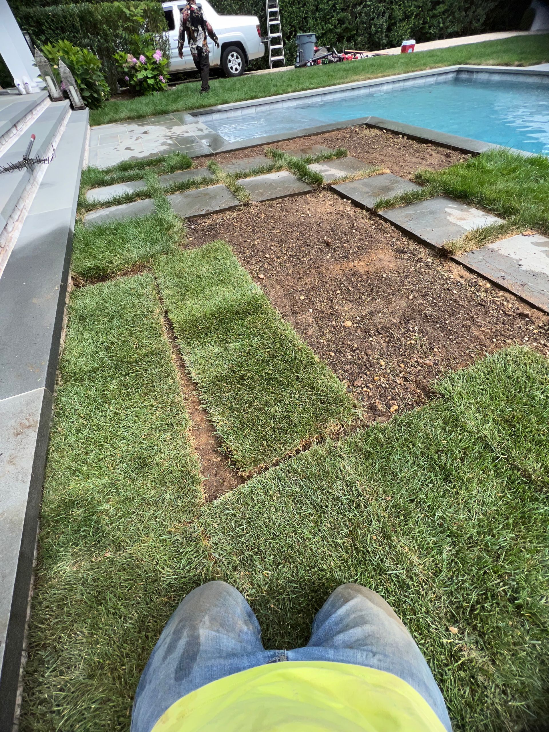A person is laying on the grass next to a pool.