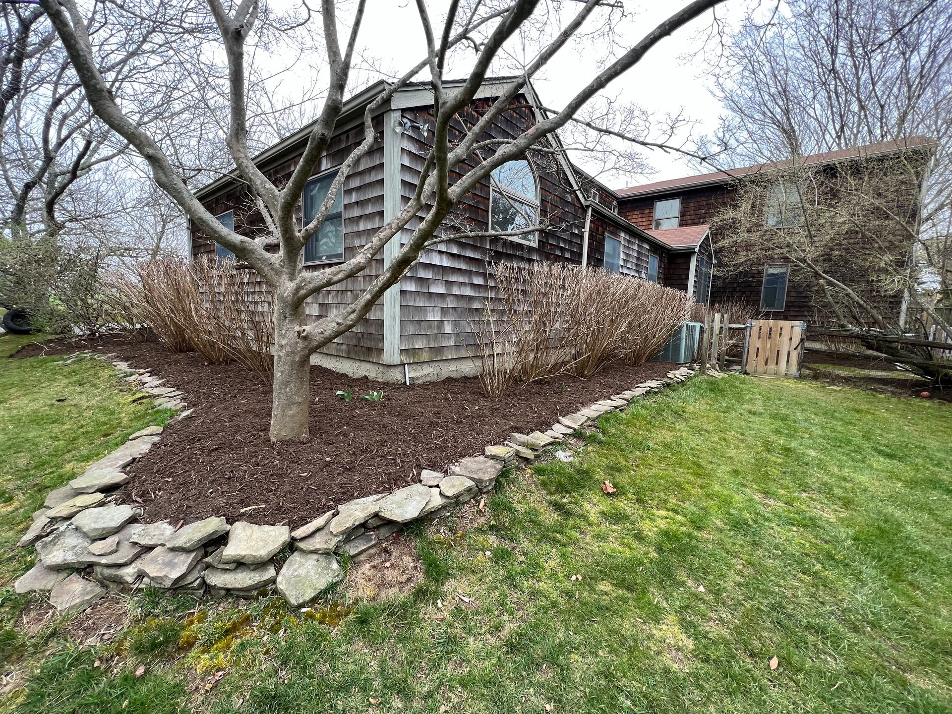 The backyard of a house with a tree in the middle of it.