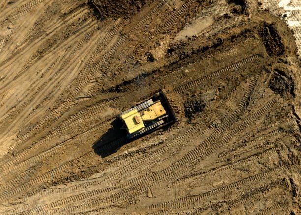 Yellow bulldozer on a construction site, pushing dirt and leaving tire tracks. Overhead shot.