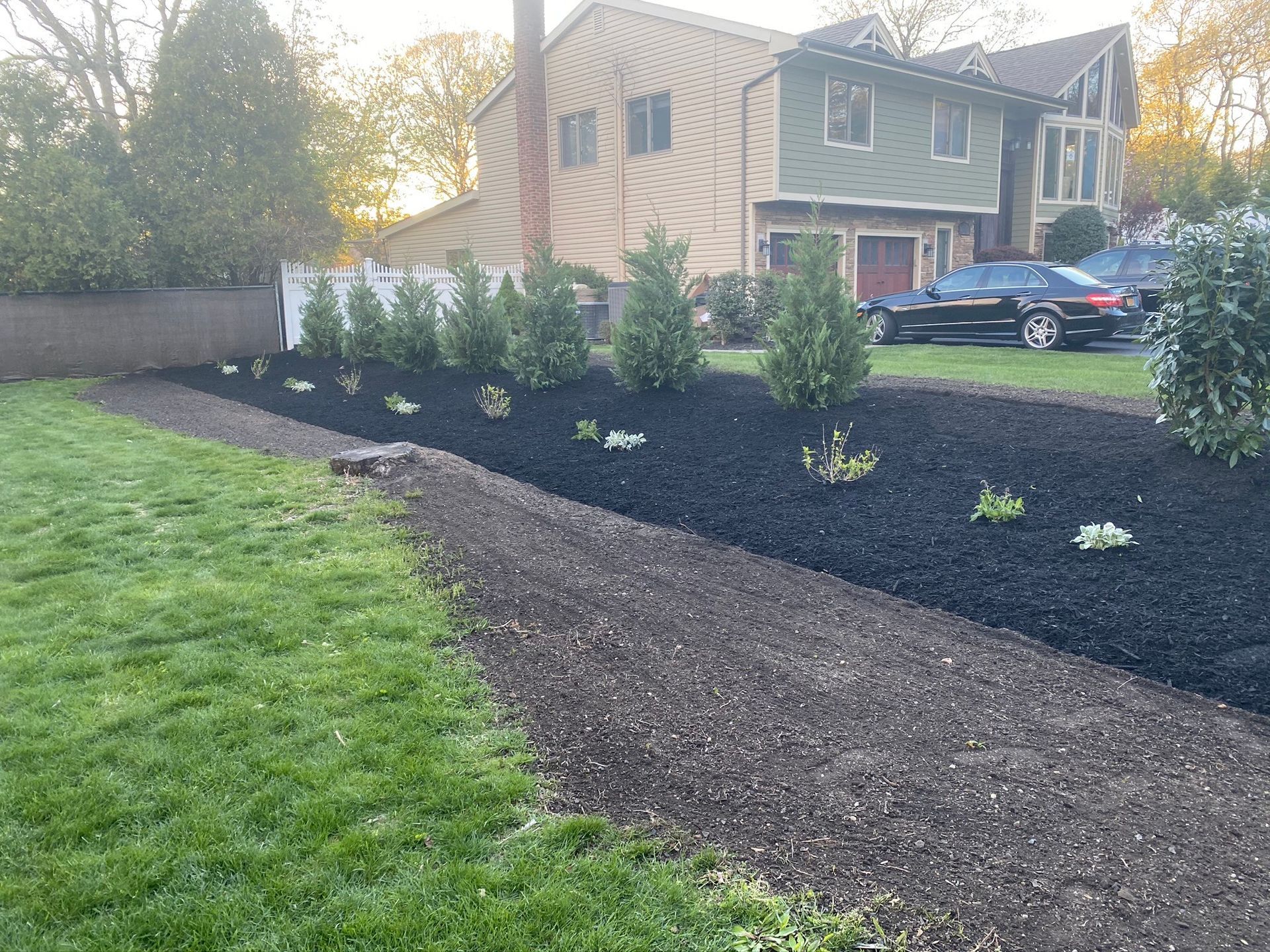 A driveway leading to a house with a lot of black mulch.