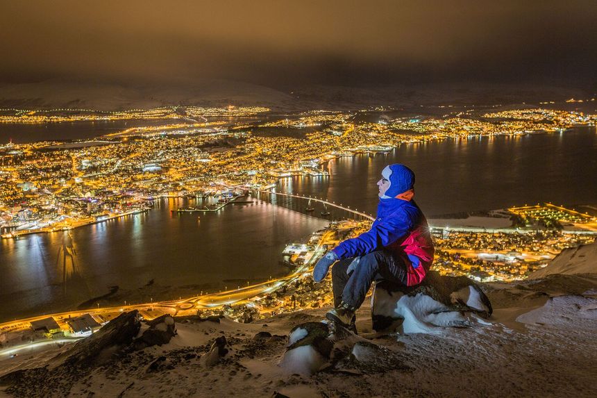 A person sitting on top of a hill overlooking Tromsø city at night