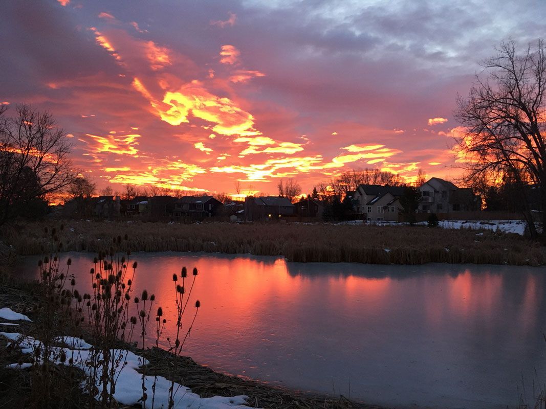 A sunset over a lake with a house in the background