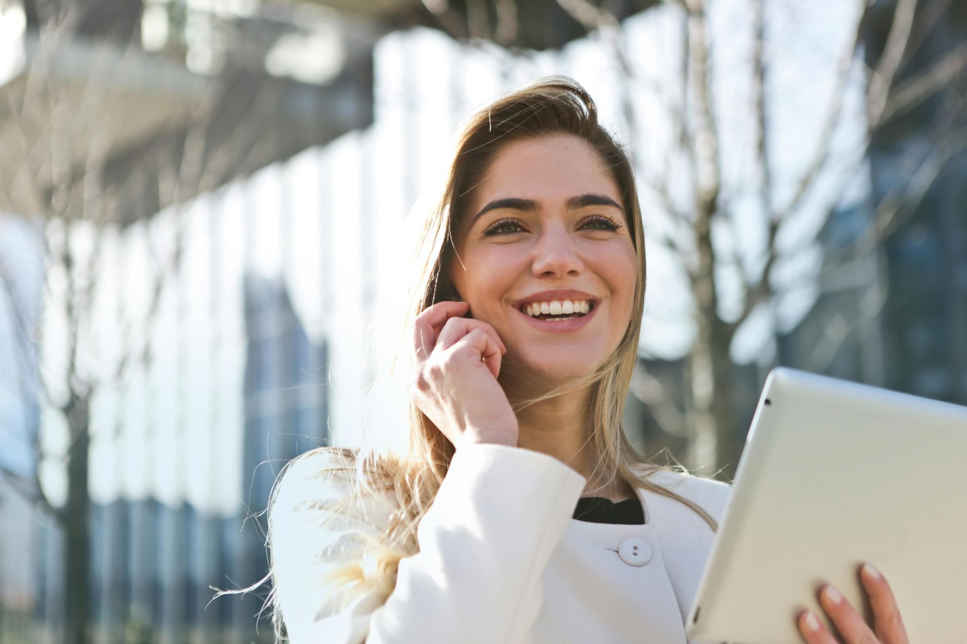 A woman is holding a tablet and talking on a cell phone.