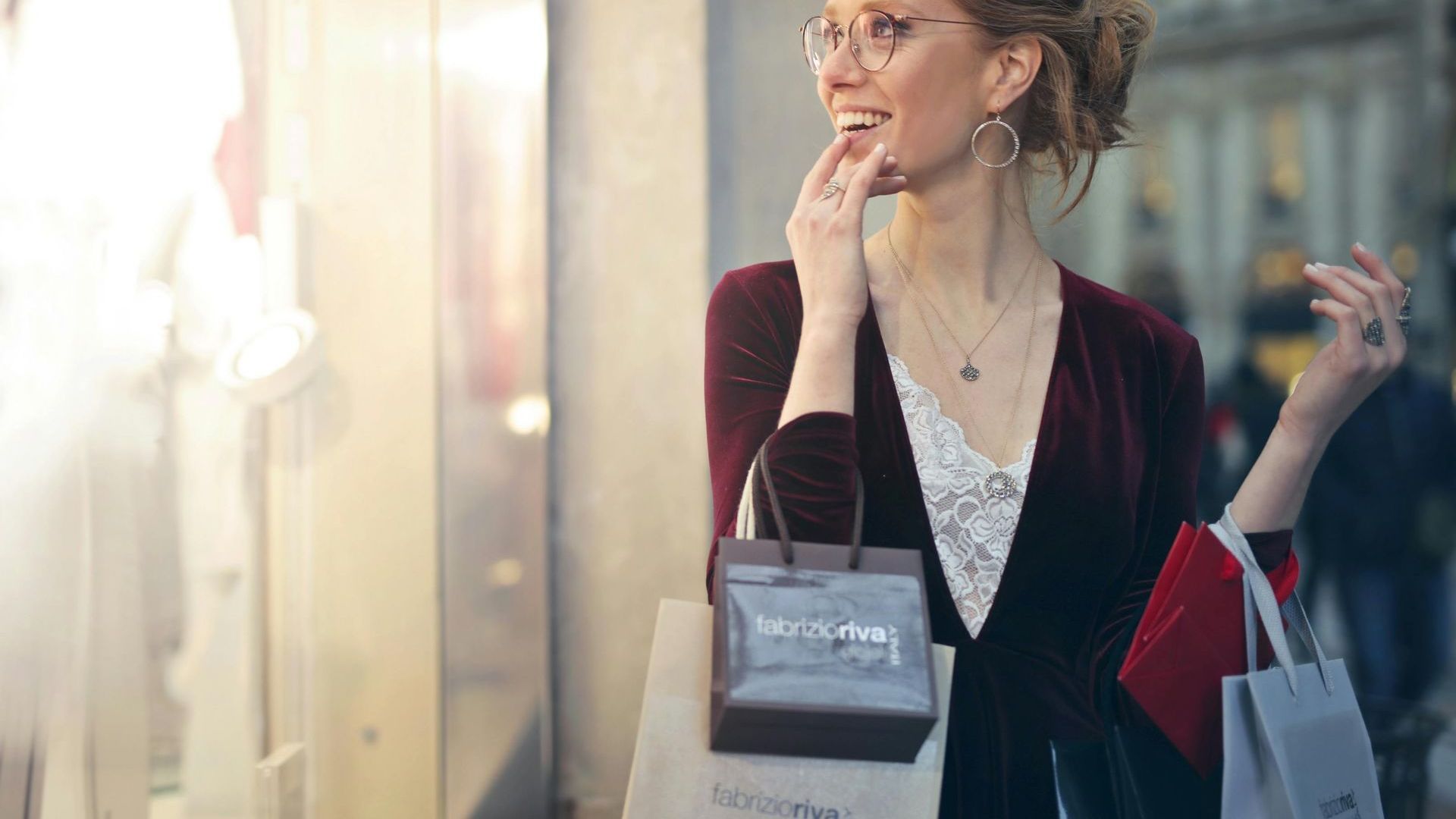 A woman is holding shopping bags and looking at a store window.