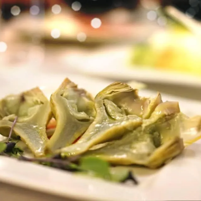 Primo piano di cuori di carciofo cotti e affettati, serviti su un piatto bianco con piccole guarnizioni verdi.