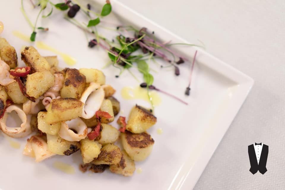 Un piatto bianco condito con patate e calamari su un tavolo.