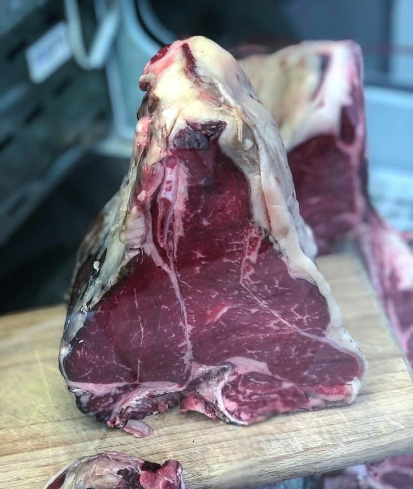 Un grosso pezzo di carne è appoggiato sopra un tagliere di legno.