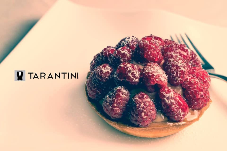 Una crostata con lamponi e zucchero a velo su un piatto bianco con una forchetta.