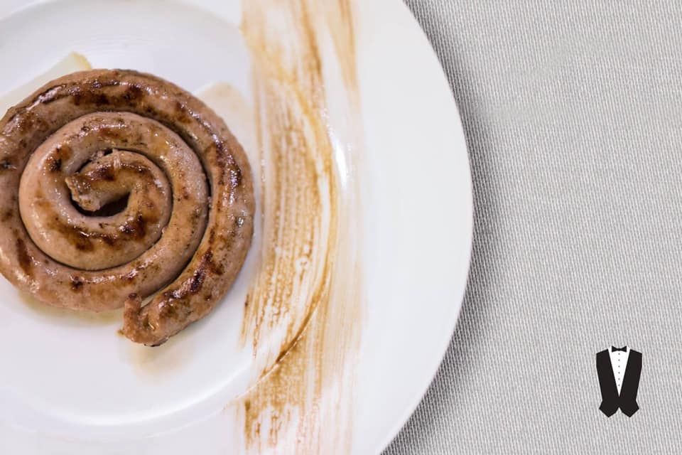 Un piatto bianco sormontato da una salsiccia a spirale su un tavolo.