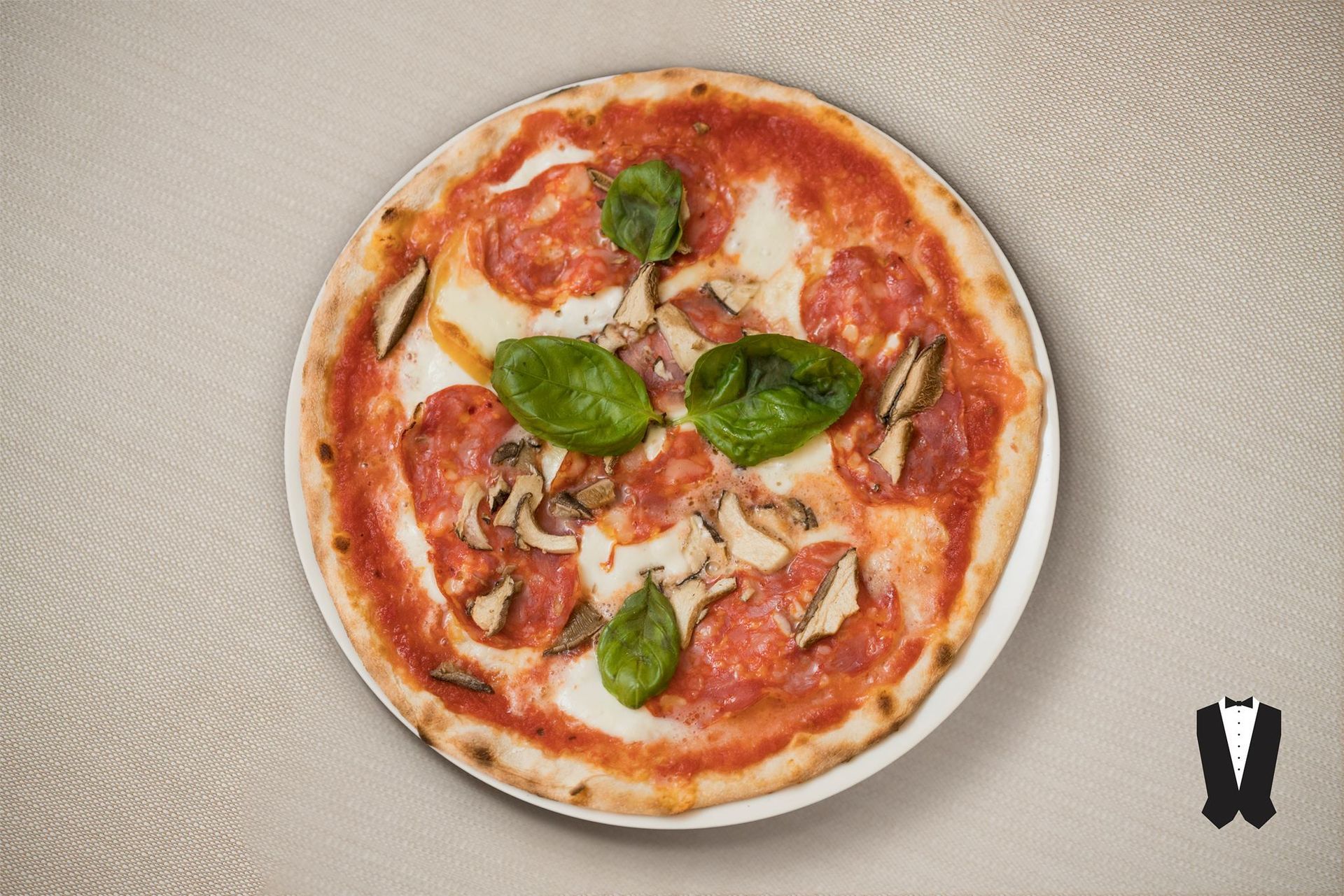 Una pizza con peperoni, funghi e basilico su un piatto bianco.