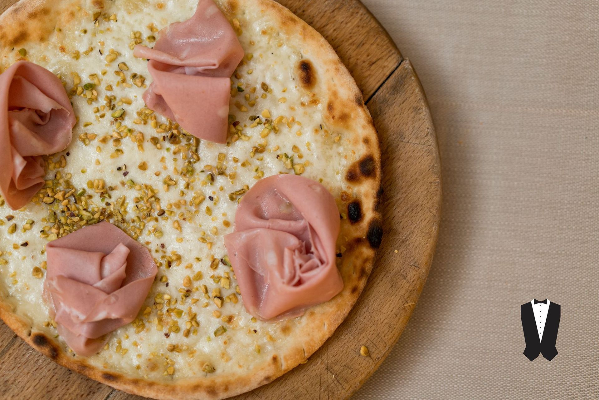 Una pizza con prosciutto e pistacchi su un tagliere di legno.