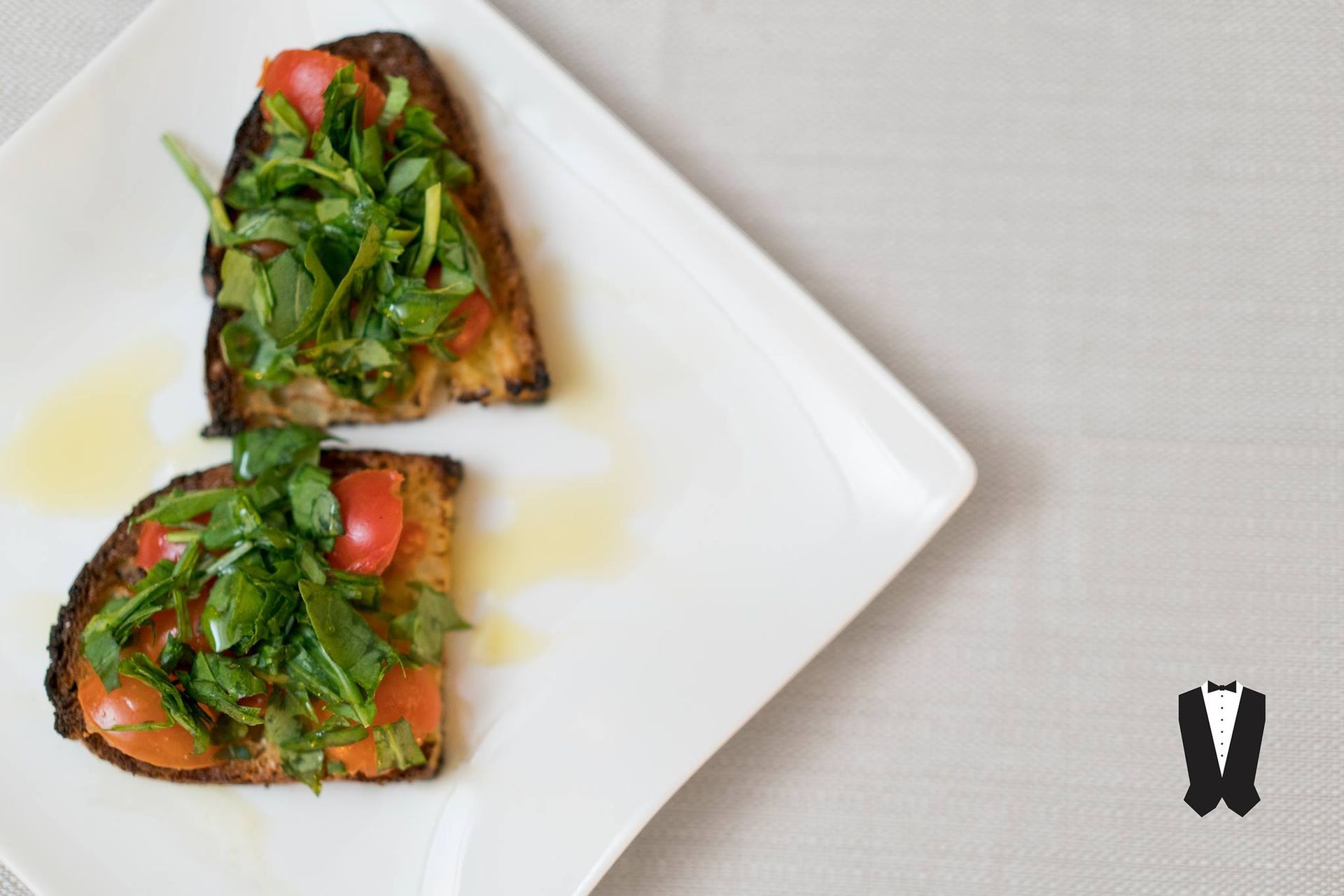 Due fette di pane tostato con pomodori e verdure su un piatto bianco.