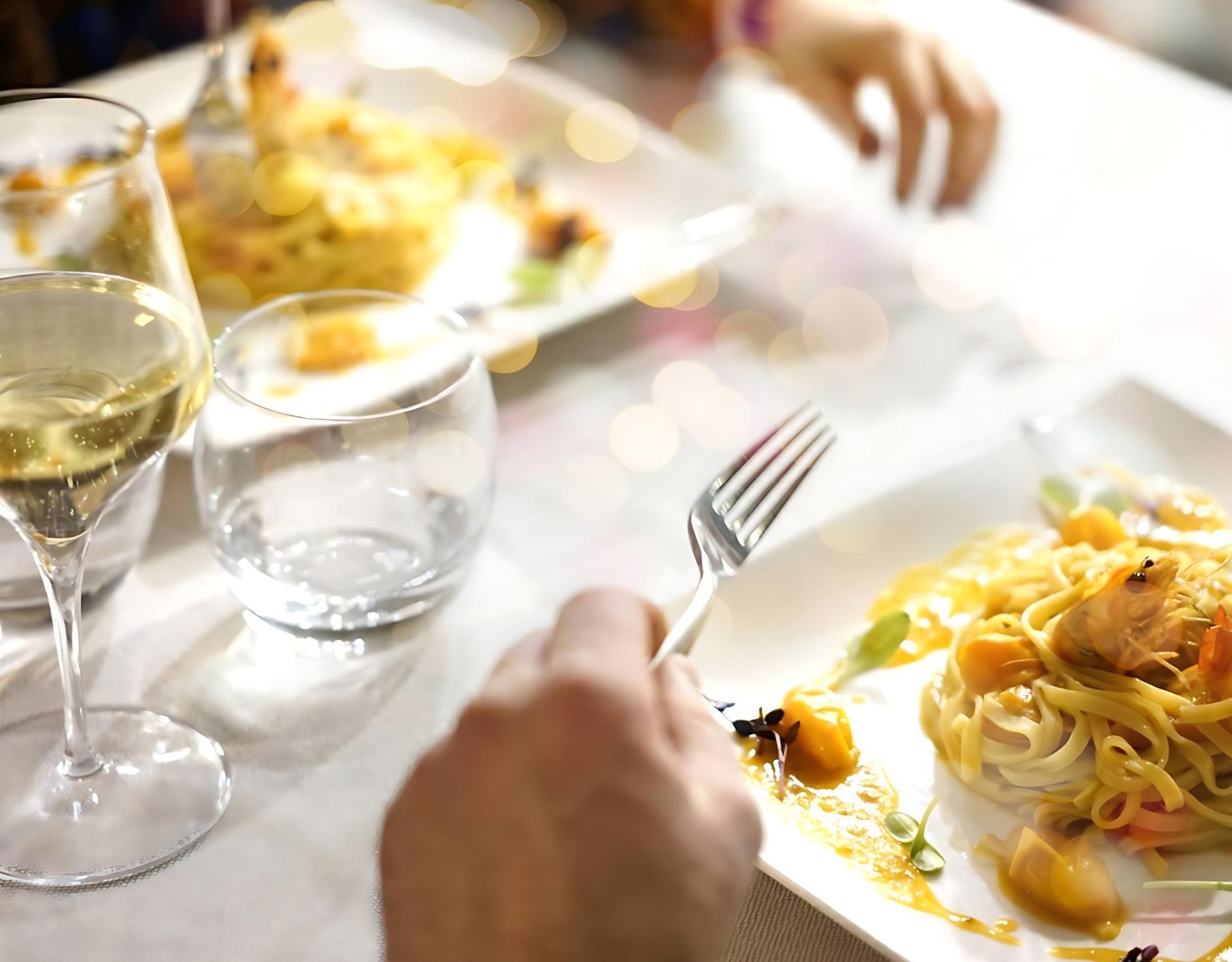 Una persona è seduta a un tavolo con un piatto di cibo e un bicchiere di vino.