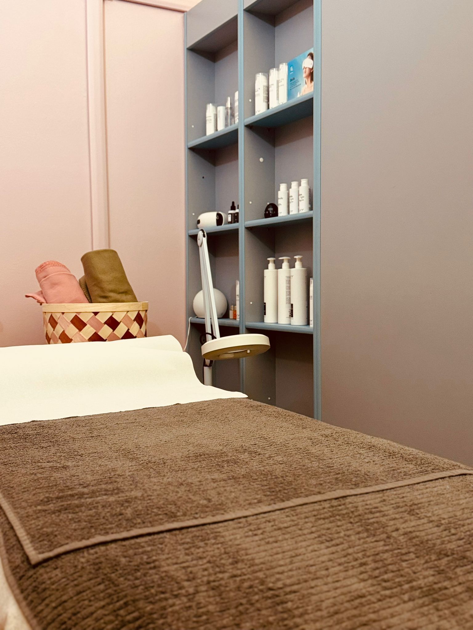 Un lettino per trattamenti con un asciugamano marrone all'interno di una sala spa, con uno scaffale pieno di prodotti per la cura della pelle.