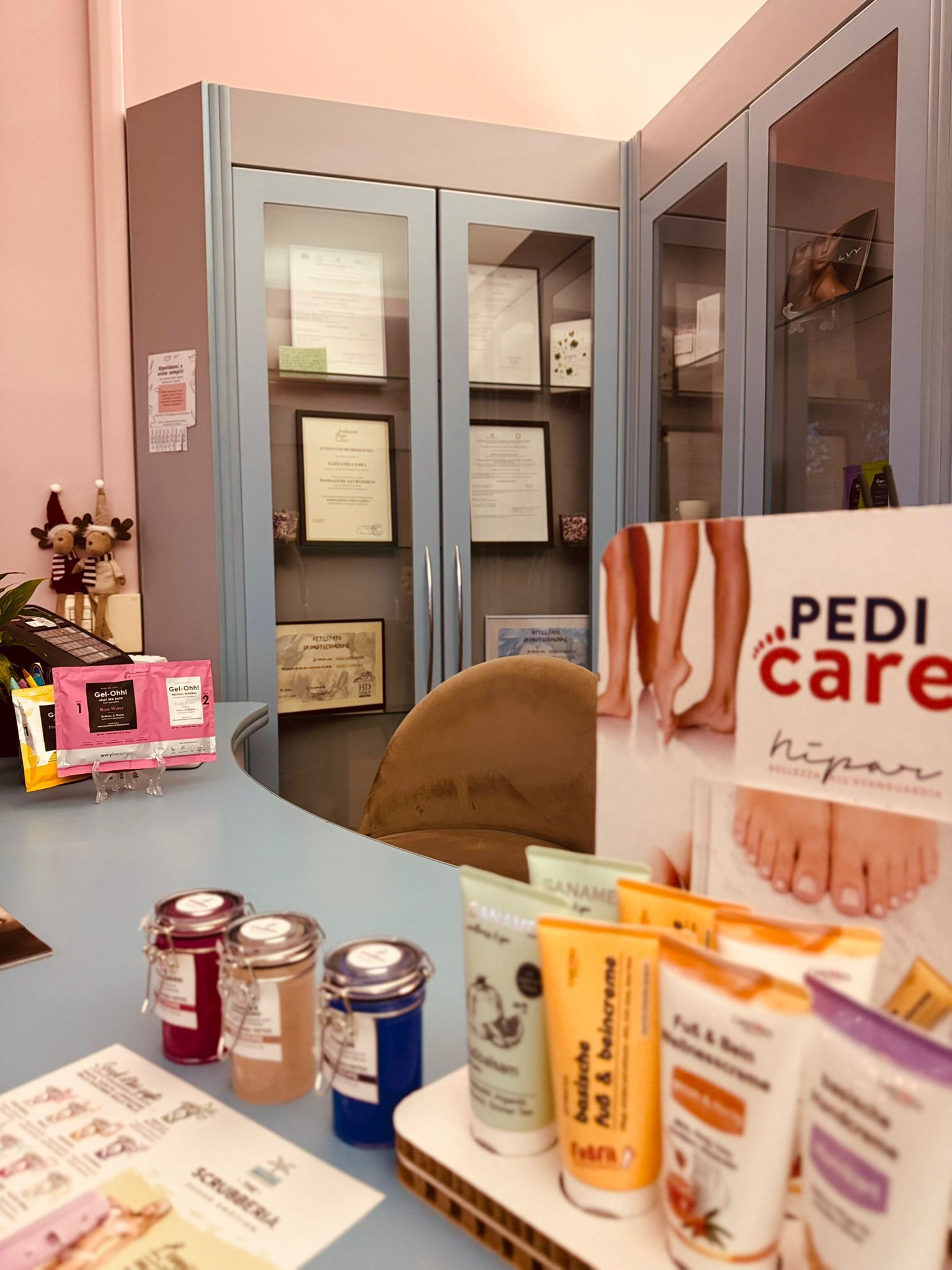 Il bancone della reception di un salone di bellezza con esposti prodotti per la cura della pelle e una pubblicità di Pedi Care davanti alle vetrine.
