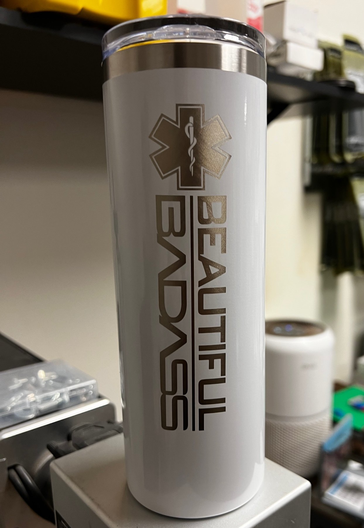 A white tumbler with the words `` beautiful badass '' on it is sitting on top of a table.