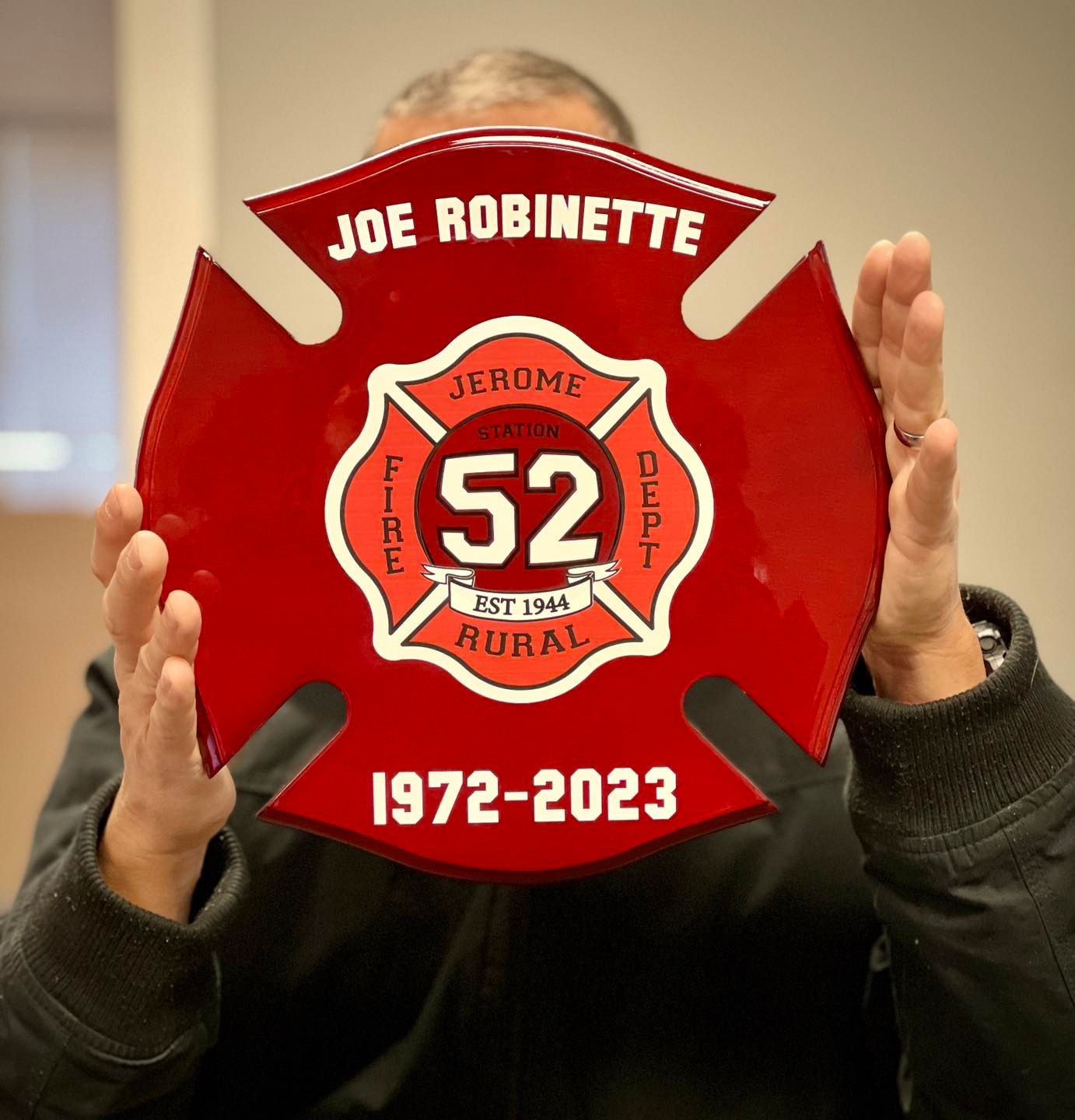 A man is holding a red fire emblem that says joe robinette 1972-2023