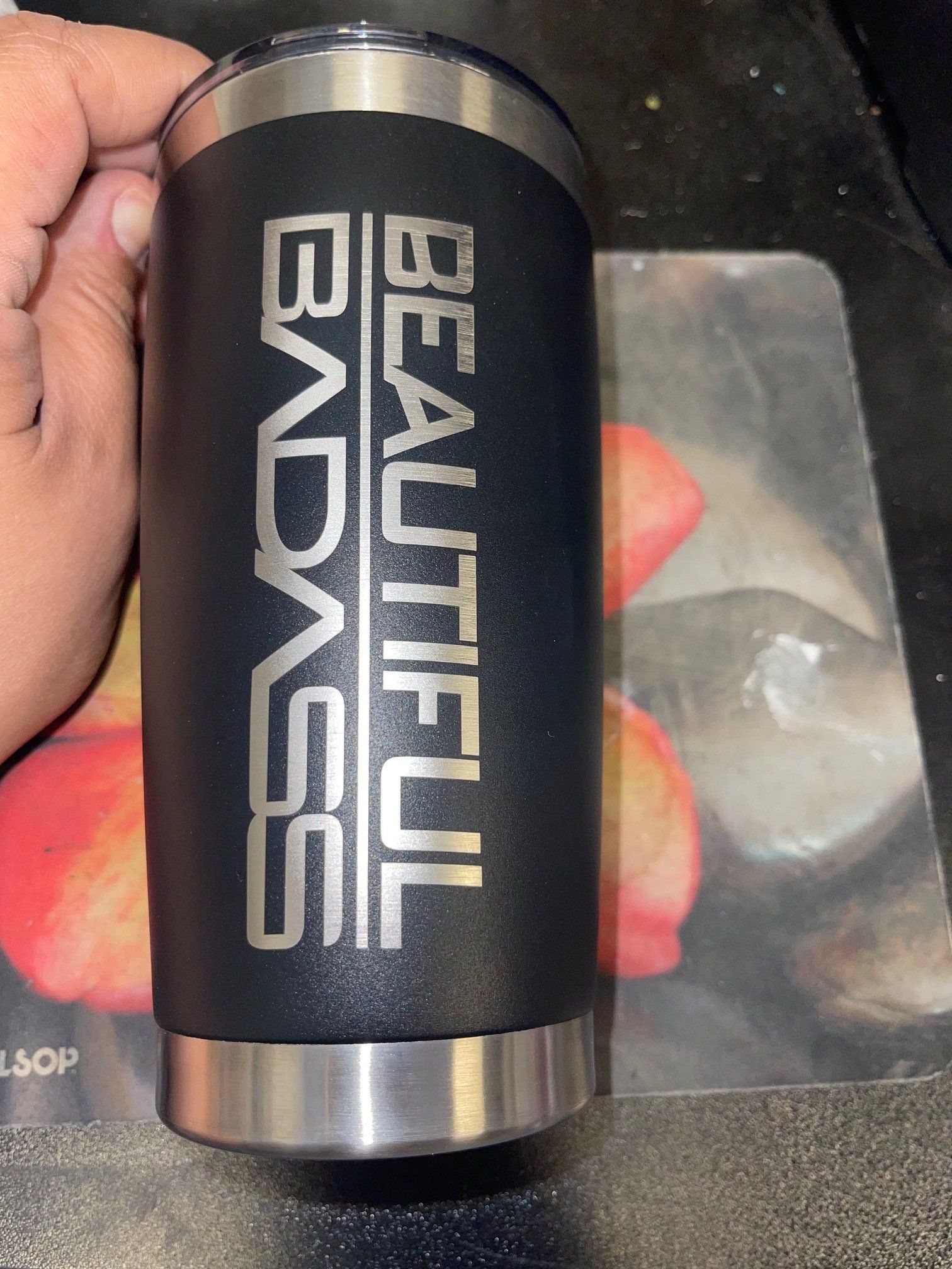 A person is holding a black tumbler that says beautiful badass on it.