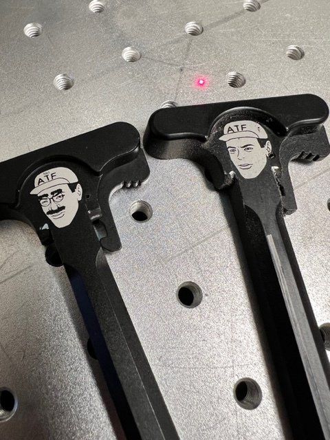 A pair of a12 ar 15 charging handles with a man 's face on them