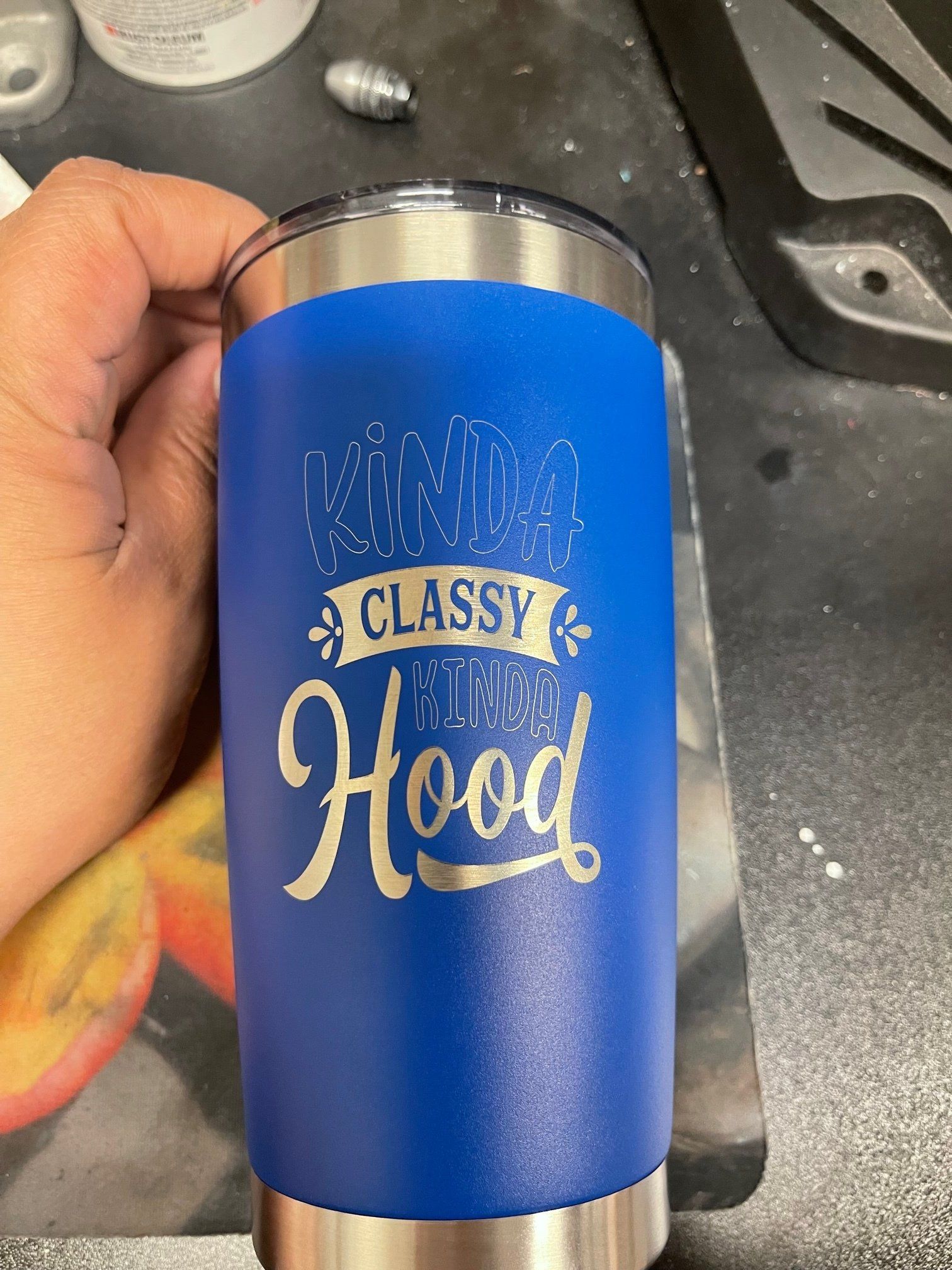 A person is holding a blue tumbler that says `` kinda classy turn hood ''.
