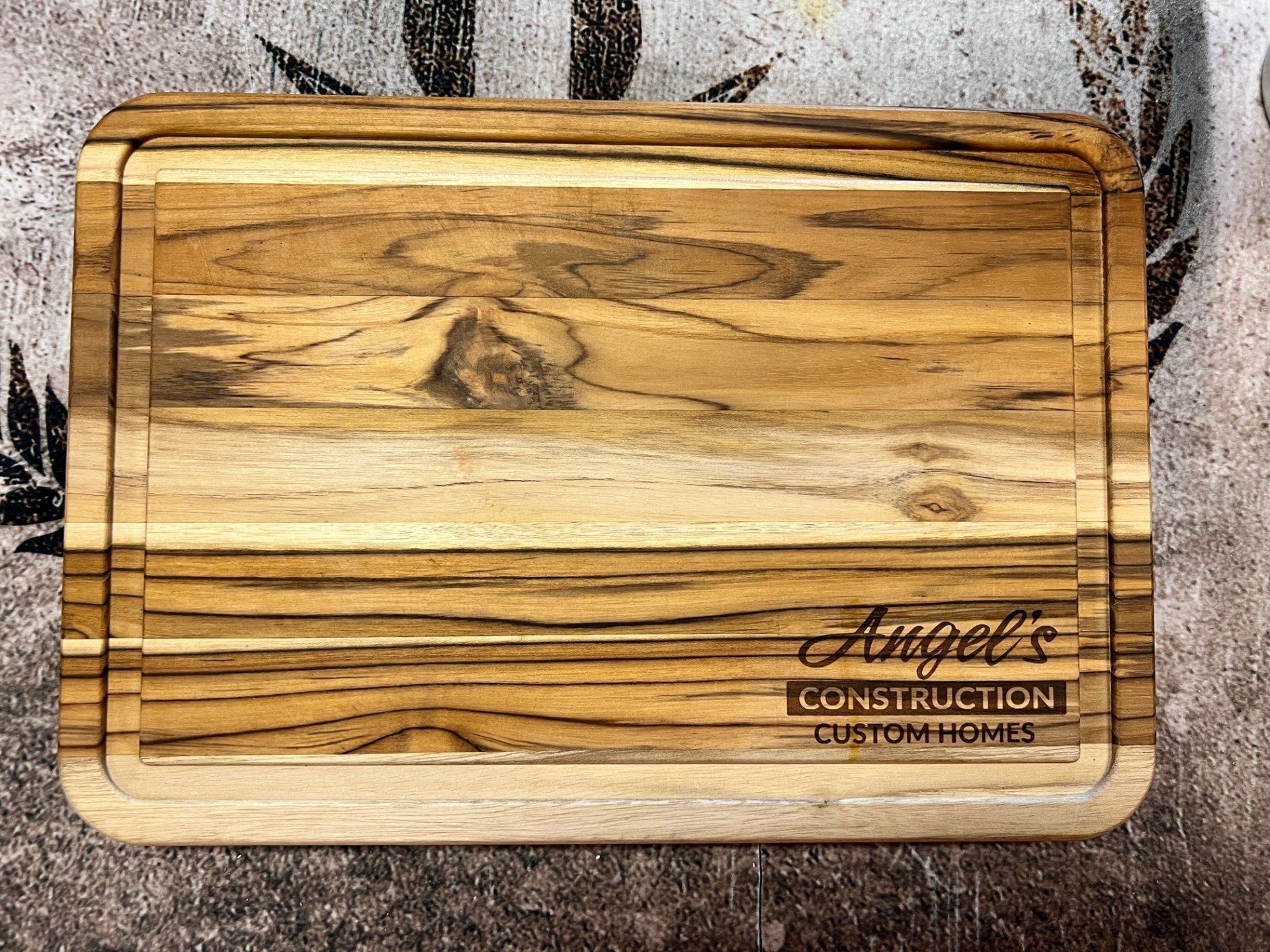 A wooden cutting board with the words `` angel 's construction custom homes '' engraved on it.