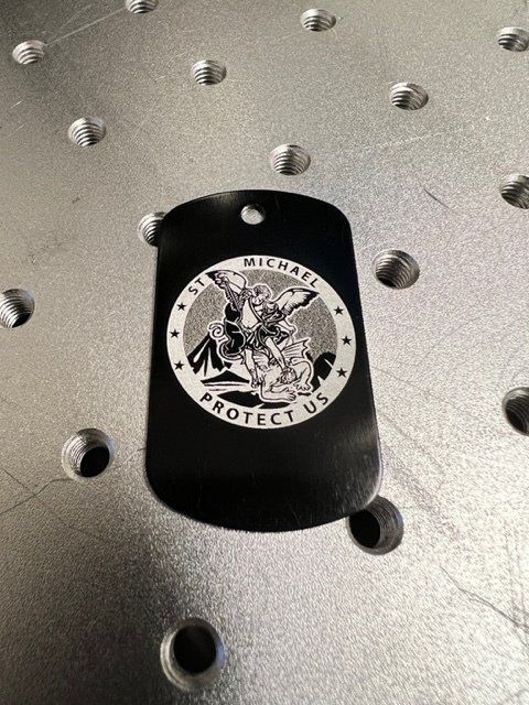 A black dog tag with a picture of michael on it is sitting on a metal surface.