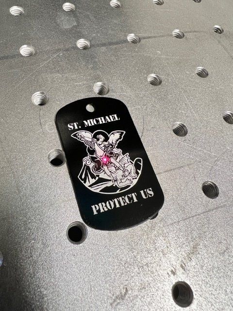 A black dog tag that says `` protect us '' is sitting on a metal surface.